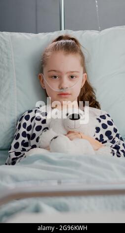 Portrait d'un petit enfant solitaire regardant dans l'appareil photo tenant un ours en dents dans les mains se reposant dans le lit souffrant d'infection. Enfant en attente d'un traitement de récupération pendant un examen médical dans la salle d'hôpital Banque D'Images