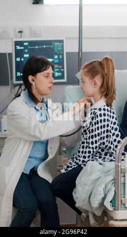 Pédiatre médecin consultant poumons à l'écoute du rythme cardiaque à l'aide d'un stéthoscope médical tandis que l'infirmière afro-américaine écrit le traitement de maladie médicalisation. Récupération des enfants dans la salle d'hôpital Banque D'Images