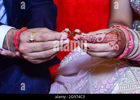 Gros plan d'une mariée et d'un marié tenant deux anneaux de mariage dans leurs mains avec le henné sur la main de la mariée Banque D'Images