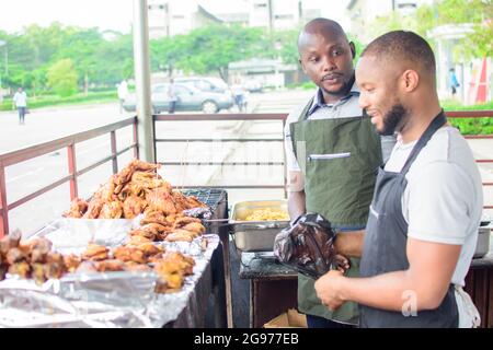 Deux vendeurs africains de barbecues et de poulets rôtis souriant et accueillant des clients pour faire patriser leur entreprise Banque D'Images