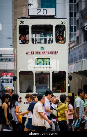 Les piétons traversent la route des Voeux, Central, Hong Kong Island, en face d'un tramway qui attend au feu rouge Banque D'Images