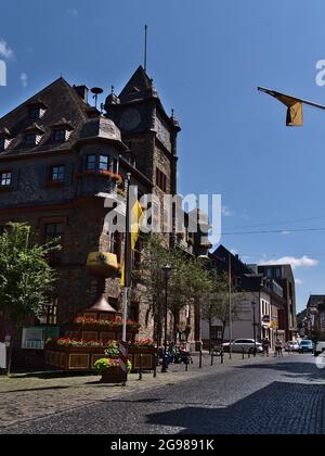 Vue sur l'hôtel de ville historique d'Oberwesel dans le centre-ville avec drapeaux, fleurs et grande sculpture de verre de vin le jour ensoleillé d'été avec ciel bleu. Banque D'Images