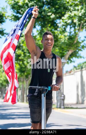 Latino homme à cheval sur un scooter électrique portant le drapeau des États-Unis Banque D'Images