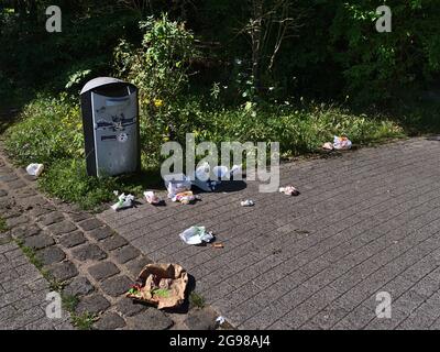 Poubelle dans la zone du parc de Koblenz avec déchets d'emballages autour de l'herbe verte et des buissons le jour d'été ensoleillé. Banque D'Images