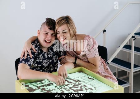 Les enfants ayant un handicap se font une activité sensorielle plateau de sable, table de sable pour l'animation, infirmité motrice cérébrale jouant au jeu apaisant, entraînement moteur fin Banque D'Images