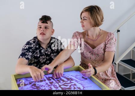 Les enfants ayant un handicap se font une activité sensorielle plateau de sable, table de sable pour l'animation, infirmité motrice cérébrale jouant au jeu apaisant, entraînement moteur fin Banque D'Images