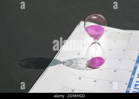 Sablier avec écoulement de sable rose et calendrier sur fond noir de plan d'examen. Copier l'espace. Banque D'Images