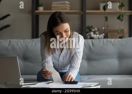 Une femme souriante gère ses finances personnelles effectue des calculs sur la calculatrice Banque D'Images