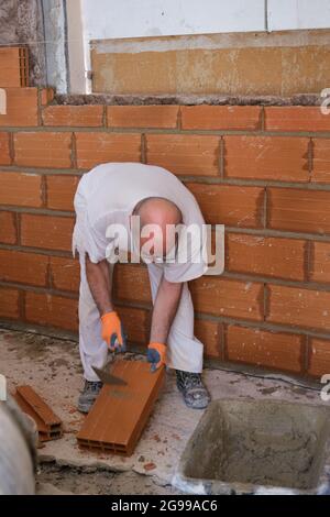 Un ouvrier de la construction casse une brique pour la faire fixer sur un mur. Homme posant des briques après avoir placé une isolation acoustique et thermique dans un mur. Homme brique Banque D'Images