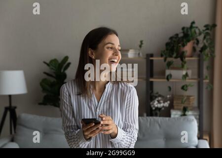 Femme gaie debout dans le salon avec un smartphone Banque D'Images