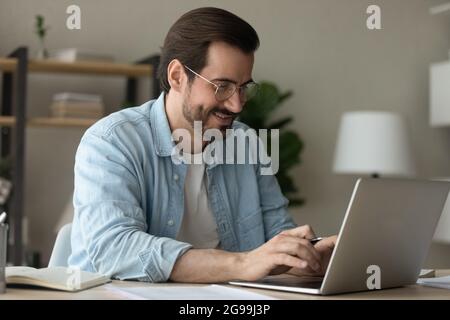 Un homme s'assoit au bureau, envoie un SMS sur un ordinateur portable qui travaille depuis son bureau Banque D'Images