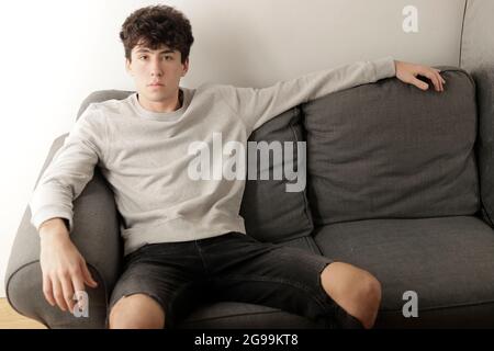 jeune homme assis confortablement sur un canapé regardant l'appareil photo Banque D'Images