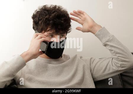 jeune homme avec masque parlant avec son téléphone mobile et expression de colère Banque D'Images