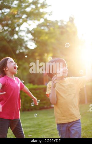 enfants latins jouant avec des bulles de savon dans le paquet avec le rétroéclairage Banque D'Images