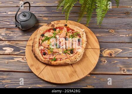 Une délicieuse pizza avec du saumon et des olives sur un stand en bois Banque D'Images