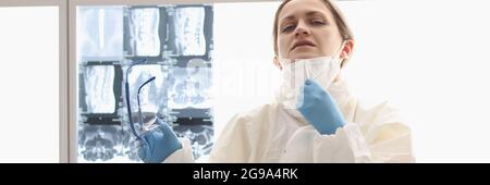 Un médecin fatigué en costume de protection est assis sur le sol avec des rayons X. en arrière-plan Banque D'Images