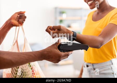 Black Lady payant par Smartwatch recevoir des articles d'épicerie de Courier à l'intérieur Banque D'Images