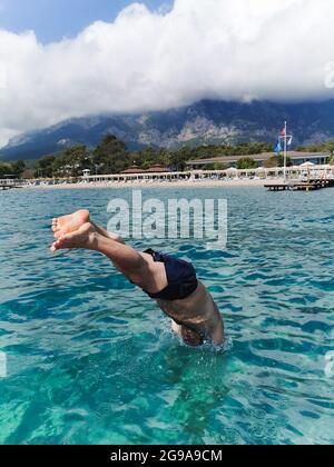 Un homme plonge en short plonge depuis une plate-forme vers la mer Banque D'Images