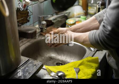 Lavage des mains dans l'évier. Le Bachelor lave ses doigts avec du savon. Lavabo sale dans la maison. De l'eau coule du robinet. Banque D'Images