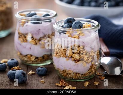 Gros plan d'un parfait de granola avec du yogourt aux bleuets et des myrtilles fraîches sur une table en bois Banque D'Images