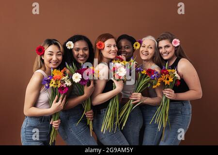 Six femmes souriantes de différents âges regardant la caméra dans un studio. Joyeux femelles diverses avec des bouquets et des fleurs dans leurs cheveux debout ensemble. Banque D'Images