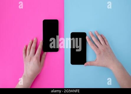 Les mains des femmes touchent deux smartphones avec écrans vierges sur fond bleu et rose, vue de dessus, plat Banque D'Images