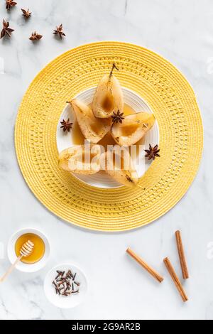 Vue de haut en bas des poires pochées et torchées avec des bâtons de cannelle, de l'anis étoilé, un bol de clous de girofle et de miel. Banque D'Images