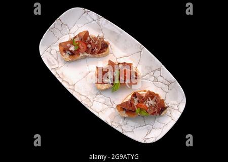 bruschetta avec prosciutto sur plaque isolée sur fond noir Banque D'Images