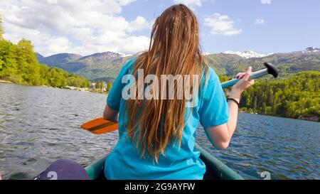 Une jeune femme fait du canoë-kayak à l'aide d'une paddle à une seule lame, en descendant un magnifique lac de montagne, vue sur l'arrière Banque D'Images