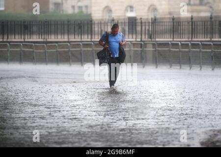 Un homme marche à travers les eaux d'inondation dans Horse Guards Road dans le centre de Londres. Les orages qui apportent des éclairs et des pluies torrentielles au sud sont sur le point de se poursuivre jusqu'à lundi, ont dit les prévisionnistes. Date de la photo: Dimanche 25 juillet 2021. Banque D'Images