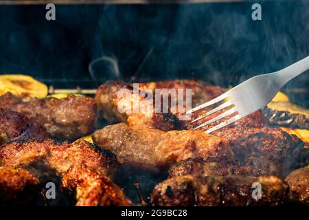 Un gros plan de rouleaux de viande de cuisson appelés mici ou mititei avec des légumes sur barbecue à l'omble Banque D'Images