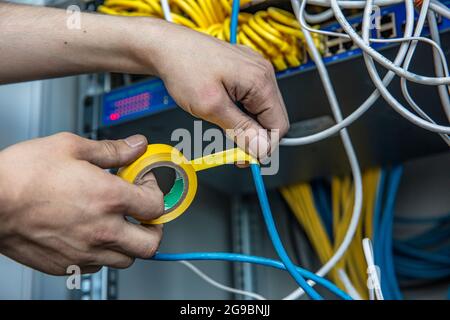 Un électricien répare le câblage dans la salle électrique à l'aide de ruban isolant. Vue rognée de l'électricien à l'aide de ruban isolant lors de la fixation des fils Banque D'Images