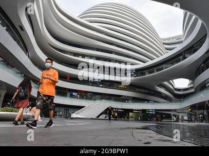 Pékin, Chine. 25 juillet 2021. Un homme portant un masque se promène près du centre commercial SOHO de la galaxie à Beijing. Le Galaxy SOHO est situé dans la 2ème route du périphérique est, près de Chaoyangmen, Beijing. Il a été achevé en 2012 et construit par Zaha Hadid Architects, Royaume-Uni, couvrant une superficie de 334000 mètres carrés (3595000 pieds carrés). (Photo de Sheldon Cooper/SOPA Images/Sipa USA) crédit: SIPA USA/Alay Live News Banque D'Images