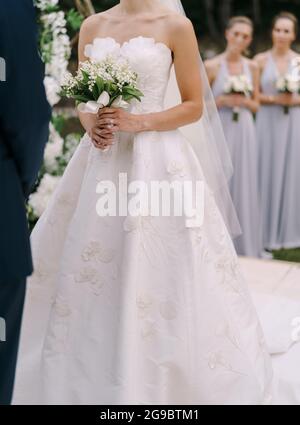 Mariée dans une robe blanche avec un bouquet dans ses mains se tient à côté du marié sur la pelouse Banque D'Images