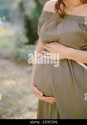 La femme enceinte en robe verte soutient le ventre avec les mains Banque D'Images
