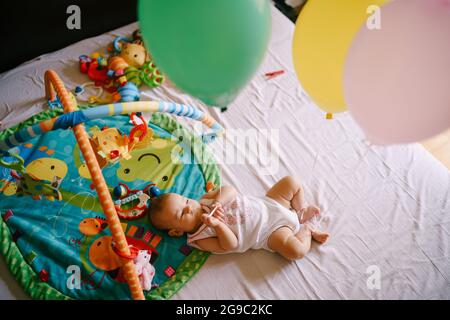 Bébé se trouve sur le lit à côté des jouets et des ballons Banque D'Images