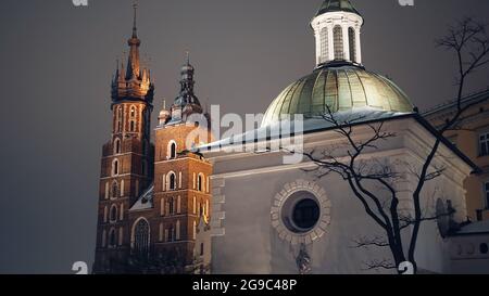 Cracovie, Pologne 03.02.2021 vue rapprochée de l'église Saint-Wojciech, place principale, Cracovie, Pologne. La tour jumelle de la basilique Sainte-Marie en arrière-plan. Des tours de grande hauteur touchent le ciel sombre. Prise de vue nocturne de haute qualité. Banque D'Images