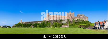 Château de Bamburgh emblématique et moulin à vent près du terrain de cricket dans le village côtier de Bamburgh dans le Northumberland, sur la côte nord-est de l'Angleterre Banque D'Images