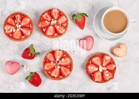 De délicieuses petites pâtisseries tartelettes garnies de fruits à la fraise et de chocolat blanc saupoudrés à côté d'une tasse de café Banque D'Images