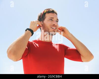 Jeune homme qui met un casque sans fil bluetooth connecté à des écouteurs SmartWatch pour courir en plein air. Bonne personne active qui porte des écouteurs pour Banque D'Images