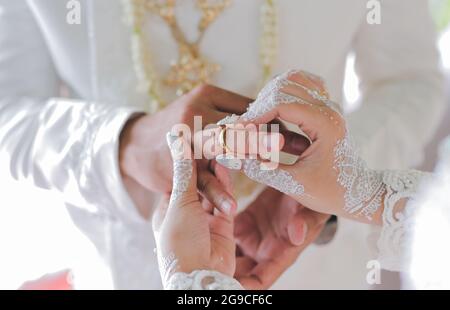 Un petit foyer d'une mariée mettant un anneau de mariage sur les mains du marié avec le tatouage blanc de henné à un mariage indonésien Banque D'Images