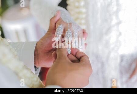 Un petit foyer d'un marié mettant un anneau de mariage sur la main de la mariée avec le tatouage blanc de henné à un mariage indonésien Banque D'Images