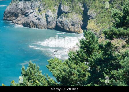 plage de rochers et d'arbres avec une mer agitée près de Cabo de Machichaco à Bilbao Espagne par une journée d'été. Banque D'Images