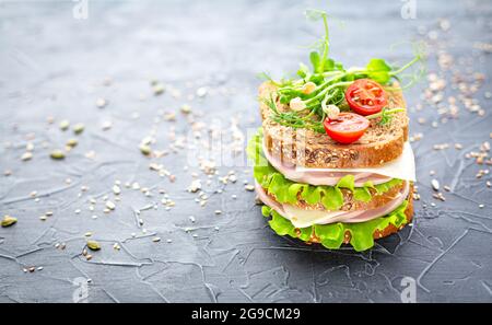 Double sandwich traditionnel de pain aux céréales avec saucisse, fromage, herbes, tomates cerises et graines de sésame sur fond texturé foncé. Déjeuner scolaire Banque D'Images