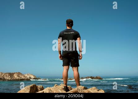 Vue arrière de l'homme qui regarde la vue sur l'océan. C'est vrai écrit sur son dos. 17 Mile Drive, Rocky Coastline, Californie, États-Unis. Septembre 2019 Banque D'Images