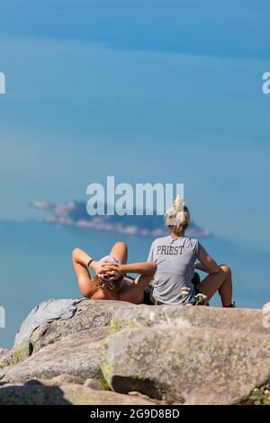 Vue rare d'un jeune couple assis sur un grand rocher tout en regardant loin sur le magnifique paysage de la mer et des îles. Parc provincial Cypress, Banque D'Images