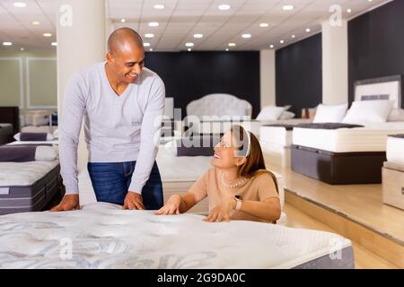 Jeune femme souriante latina avec son petit ami choisissant un nouveau matelas orthopédique moderne dans la boutique de meubles Banque D'Images