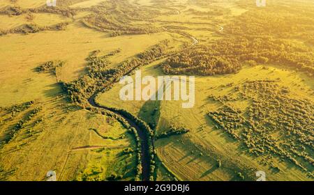 Champs et petite rivière étroite sinueuse vue aérienne. Vert paysage rural de drone dans la lumière du coucher du soleil. Concept de nature, de durabilité et d'écologie Banque D'Images