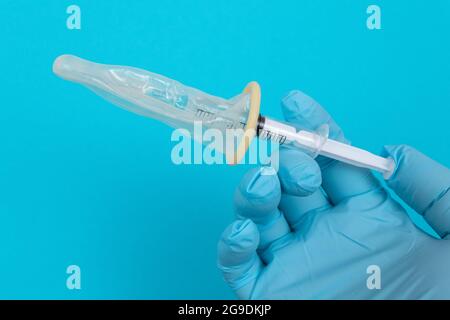 Vaccin sûr, anti-vaccin concept - seringue dans un condom tient dans une main avec un gant médical. Méfiance à l'égard de la vaccination. Immunité naturelle. Scepticisme à propos du vaccin. Liberté et droits de l'homme Banque D'Images