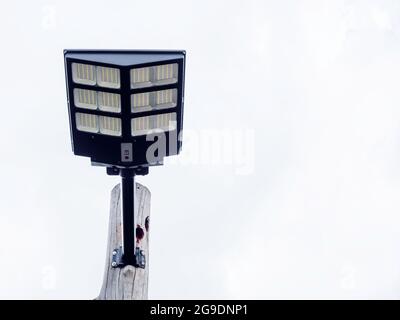 Lumière solaire montée sur un poteau en bois sur fond bleu ciel avec espace de copie. Lampadaire avec panneau solaire, vue de dessous. Banque D'Images